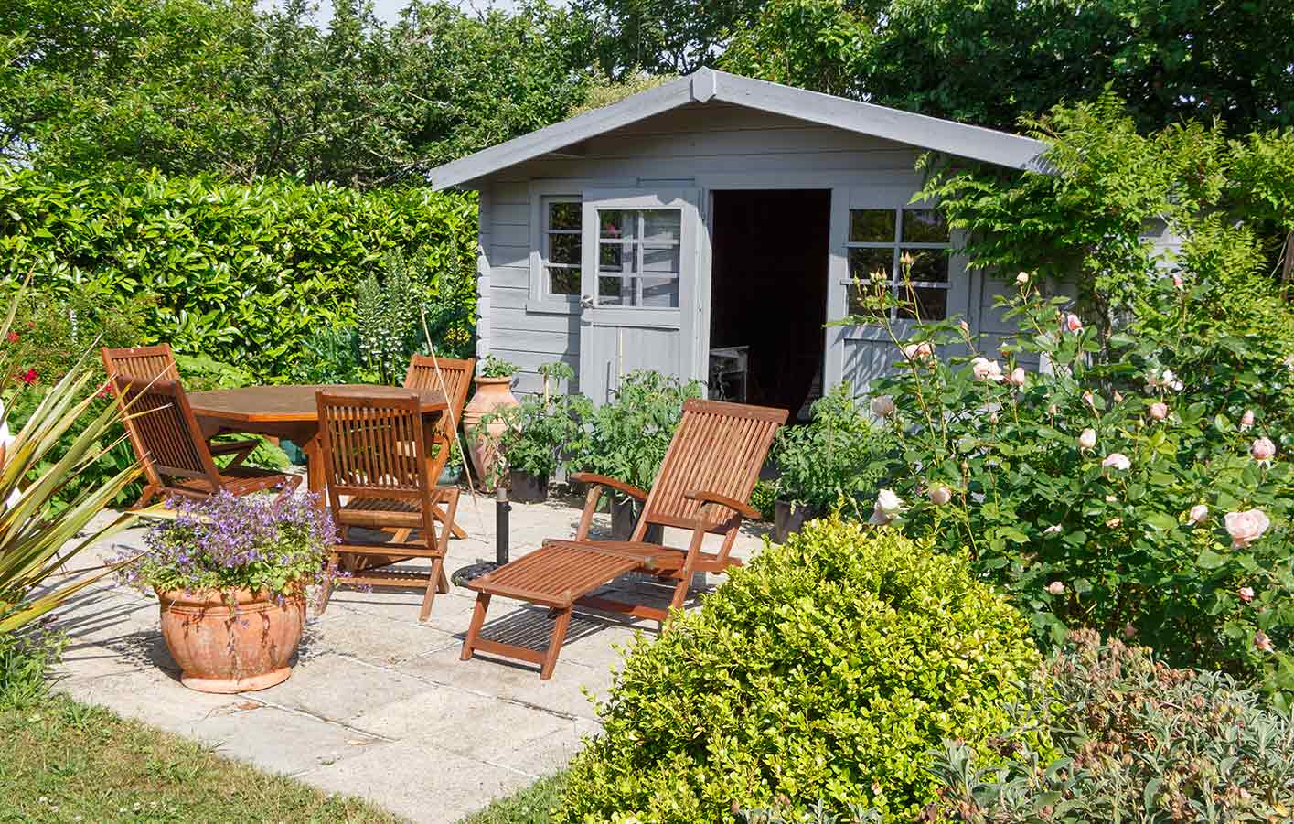 Gartenmöbel aus MAssivholz vor einer Gartenhütte aus Holz mit Spitzdach