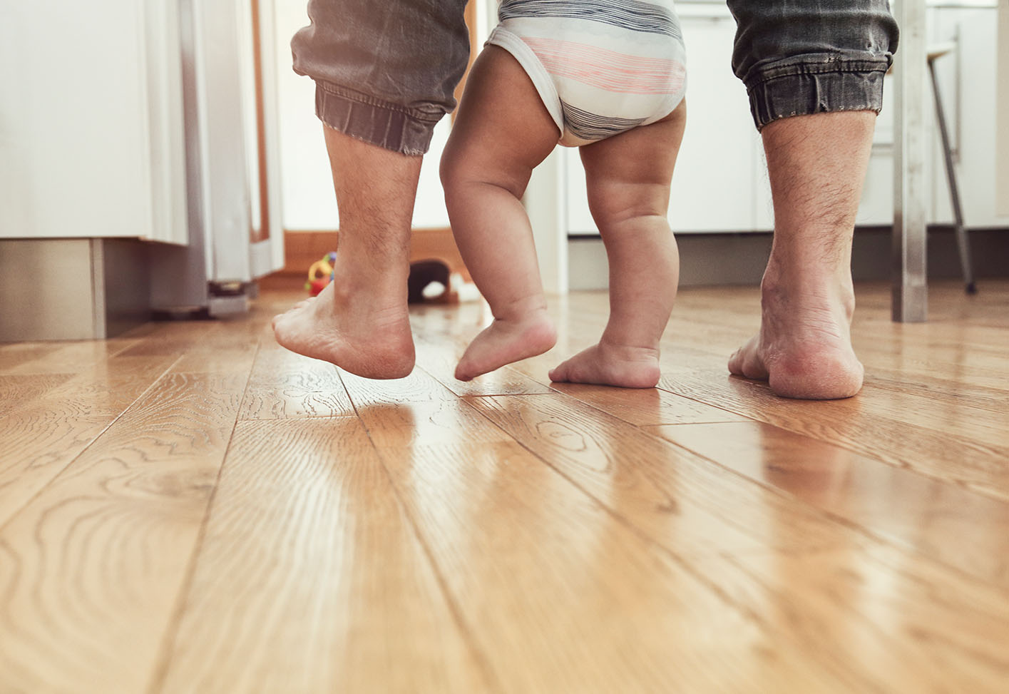 Füße von einem Vater und seinem Kind auf einem Holzboden