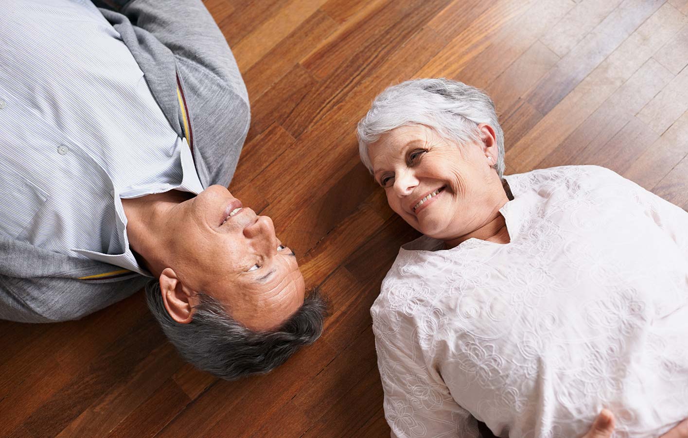 Ehepaar liegt auf einem Boden aus Furnierparkett und lächelt sich an