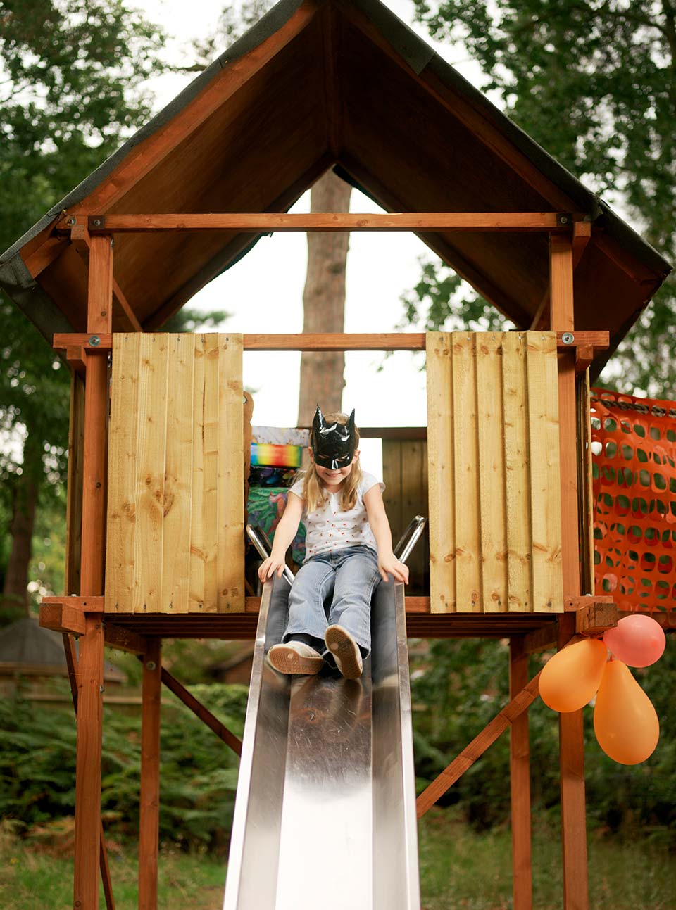 Kind rutscht auf einer Rutsche an einem Spielturm aus Holz
